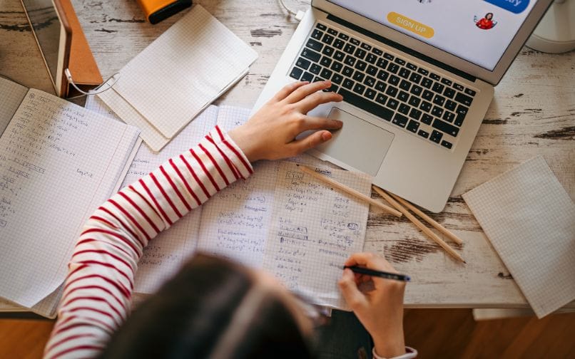 student working on a computer and taking notes on a notepad