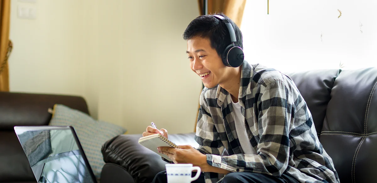 Student taking notes at home wearing a black pair of headphones